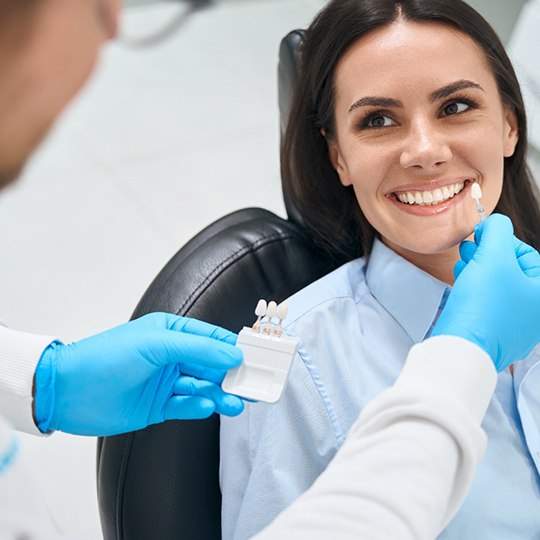 Dentist holding shade guide to woman’s teeth