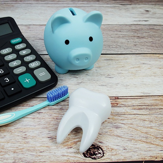Model tooth, toothbrush, piggy bank, and calculator on wooden surface