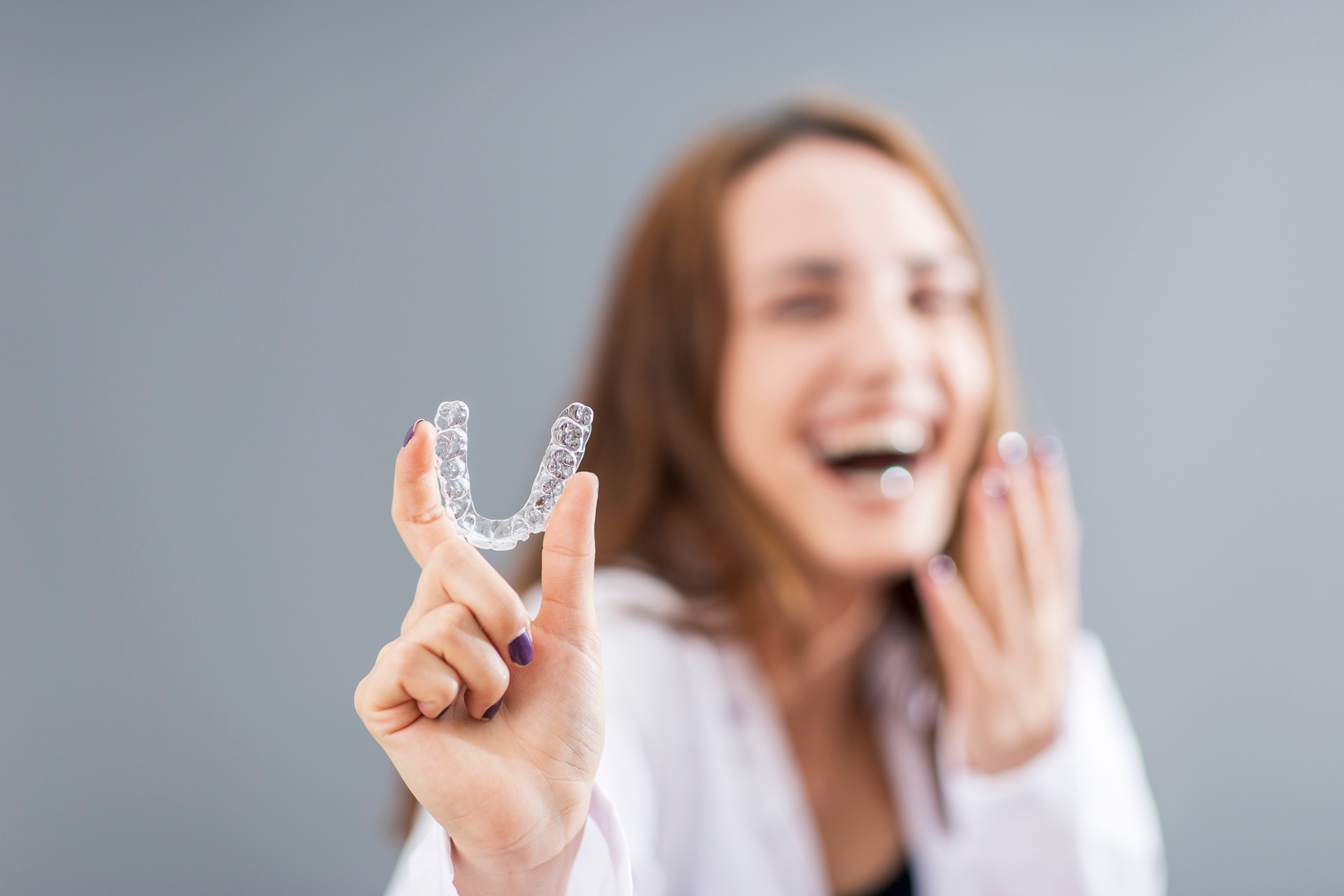 Woman is holding an Invisalign clear aligners in a studio with grey background